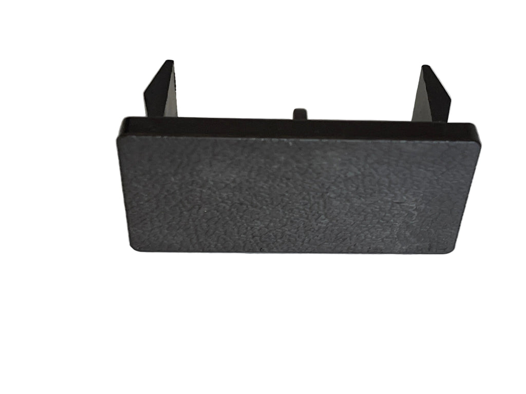 A black textured plastic rectangular bracket or cover with two small upright tabs on the top, shown on a light gray surface.