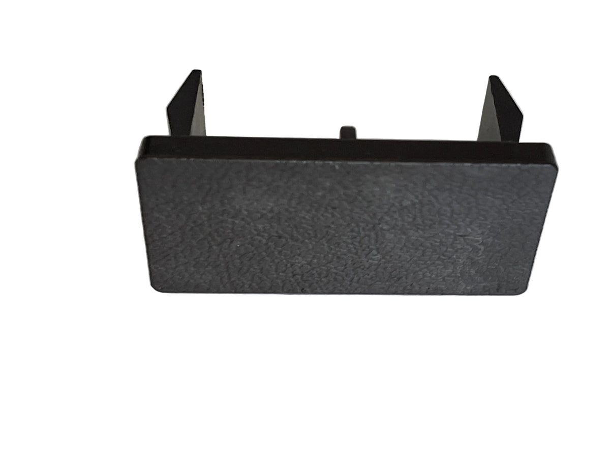 A black textured plastic rectangular bracket or cover with two small upright tabs on the top, shown on a light gray surface.